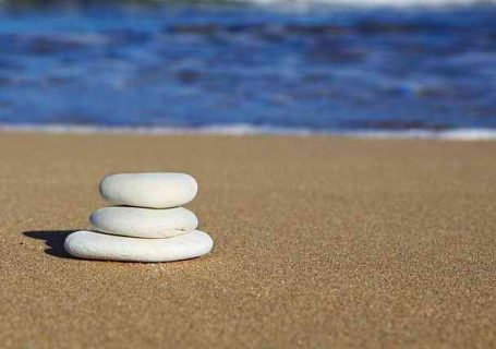 3 flache Steine als Stapel am Strand vor dem Meer im Hintergrund